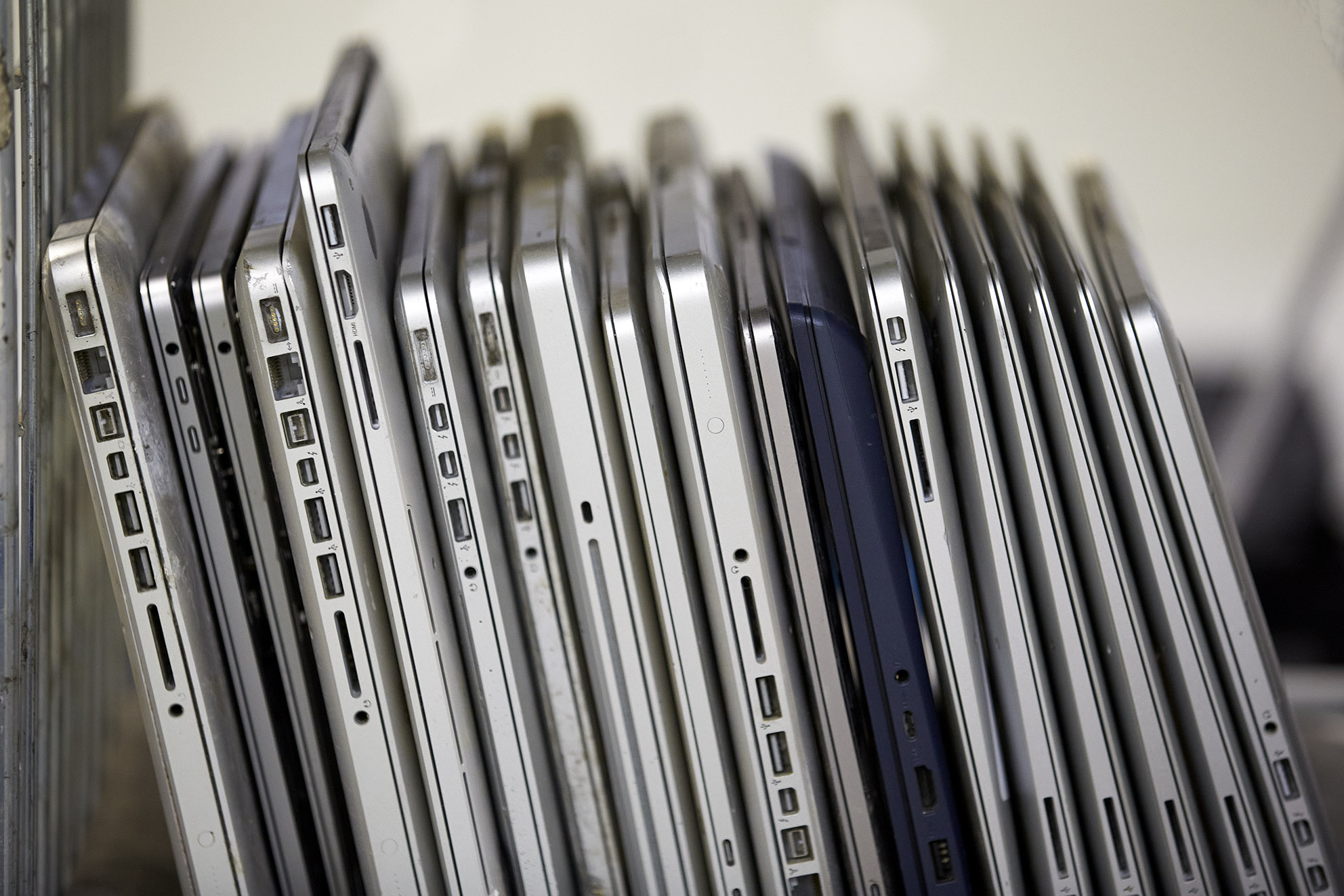 A collection of stacked laptops, showing their ports and sides, arranged vertically in a storage area.